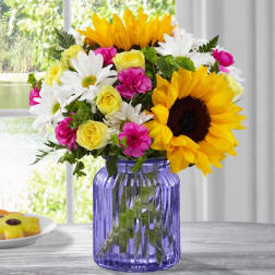 Sunflowers, white daisies, yellow roses, and pink carnations in a purple glass vase