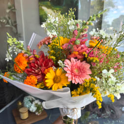 Handheld bouquet of mixed pink, yellow, orange, and white flowers wrapped in white paper