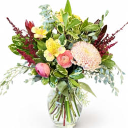 Mixed bouquet of pink and yellow flowers in a clear glass vase