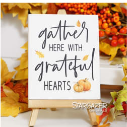 Fall sign on a small wooden easel reading "gather here with grateful hearts"