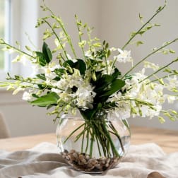 White orchid arrangement in a round glass vase with pebbles