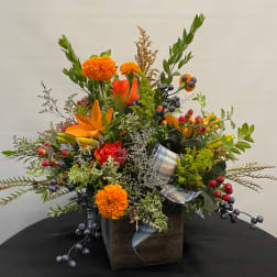 Orange and red floral arrangement in a dark wooden box with plaid ribbon