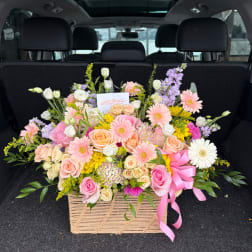 Large mixed flower arrangement in a woven basket with a pink ribbon