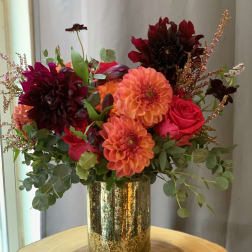 Bright mixed bouquet in a gold vase with orange, red, and dark burgundy blooms