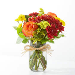 Bouquet of orange roses, red chrysanthemums, and yellow mums in a glass jar vase