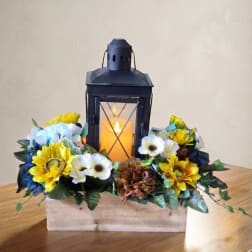 Lantern centerpiece surrounded by yellow and white flowers in a wooden box