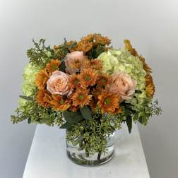 Orange and blush flowers in a clear glass vase with pale green hydrangeas