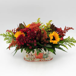 Autumn floral arrangement with sunflowers and red mums in a pumpkin-decorated container.
