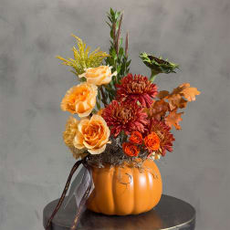 Autumn floral arrangement in an orange pumpkin container with roses and mums