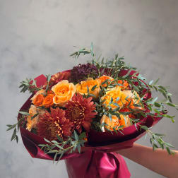 Bouquet of orange roses and burgundy chrysanthemums wrapped in magenta paper
