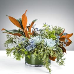 Low arrangement of blue succulents and orange foliage in a glass vase