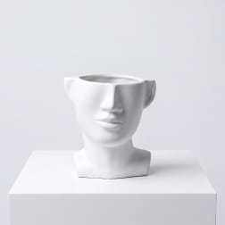 White face-shaped ceramic planter on a white pedestal