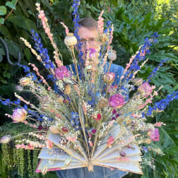 Person holding a fan-shaped floral arrangement with pink and blue dried flowers
