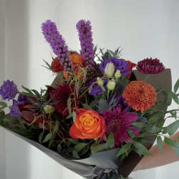 Mixed bouquet with orange and purple flowers wrapped in dark paper