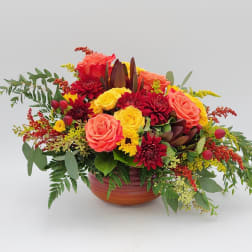 Mixed bouquet of roses and red blooms in a low ceramic bowl