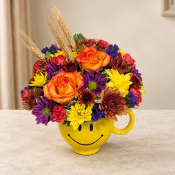 Colorful bouquet in a yellow smiley-face mug with orange roses and daisies