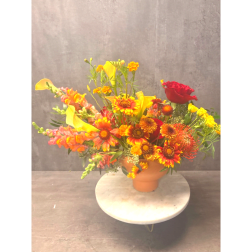 Bright mixed flower arrangement in a peach vase with red and yellow blooms
