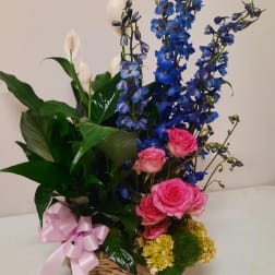 Pink roses and blue delphinium in a basket with a pink ribbon