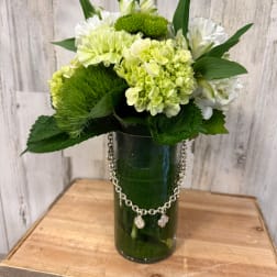 Green and white floral arrangement in a tall glass vase with a chain accent