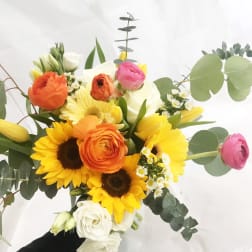 Mixed bouquet with sunflowers, roses, and ranunculus in white and yellow.