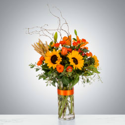 Orange and yellow bouquet in a clear glass vase with tall branches