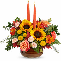 Autumn floral arrangement with sunflowers, roses, carnations, and two orange candles in a bowl vase.