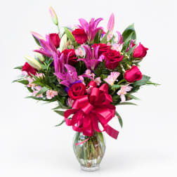 Bouquet of pink lilies and red roses in a clear glass vase with a pink ribbon