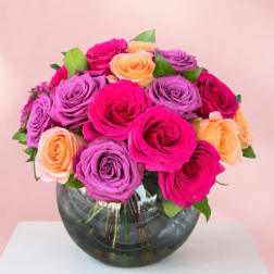 Bouquet of pink, purple, and peach roses in a round glass vase