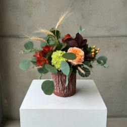Mixed bouquet in a textured brown vase with peach, red, and green blooms