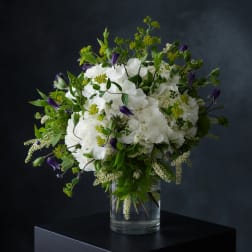 White hydrangea bouquet with purple bell-shaped flowers in a clear glass vase