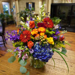 Colorful mixed bouquet in a glass vase with roses, gerberas, and blue hydrangea