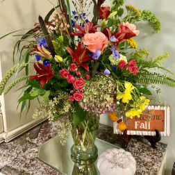 Tall mixed bouquet in a glass vase with roses, lilies, and bright fall colors