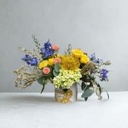 Colorful bouquet in a white floral vase with yellow, blue, pink, and green blooms