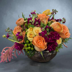 Mixed bouquet of orange, yellow, and purple flowers in a low bowl vase