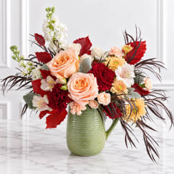 Peach roses and mixed flowers in a green ceramic pitcher vase