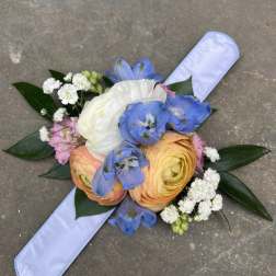 Hand-tied bouquet with blue, white, and peach flowers on a pale ribbon
