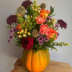 Mixed bouquet in a carved pumpkin vase with orange roses and burgundy blooms