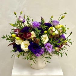 Purple, white, and yellow flowers in a ribbed white vase