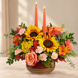 Sunflower and rose arrangement with two orange taper candles in a glass bowl