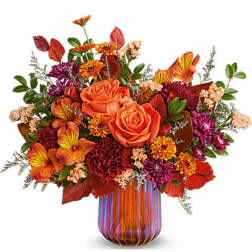 Orange roses and mixed fall flowers in a striped glass vase