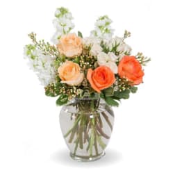 Peach and orange roses arranged in a clear glass vase with white blooms