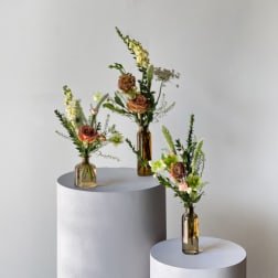 Three small floral arrangements in amber bottles with mixed blooms