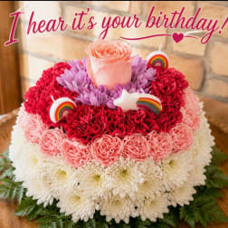 Round floral cake with pink, red, and white blooms and birthday topper