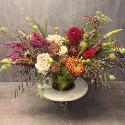 Large mixed floral arrangement in a dark vase with cream, red, and orange blooms