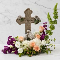 Floral arrangement with peach and white roses around a decorative cross and bird figurines