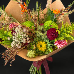 Mixed bouquet with bright orange, pink, yellow, and green flowers wrapped in brown paper