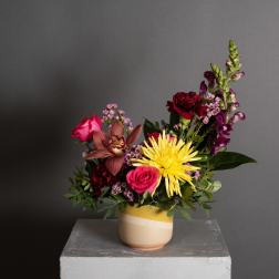 Mixed bouquet in a striped ceramic vase with pink, red, yellow, and purple blooms