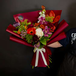 Mixed bouquet with roses, orchids, and bright autumn flowers wrapped in burgundy paper
