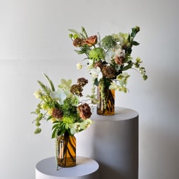 Two floral arrangements in amber glass vases on round pedestals