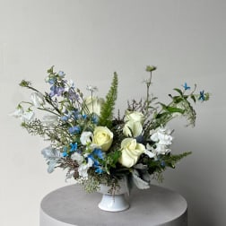 White and blue floral arrangement in a white pedestal vase